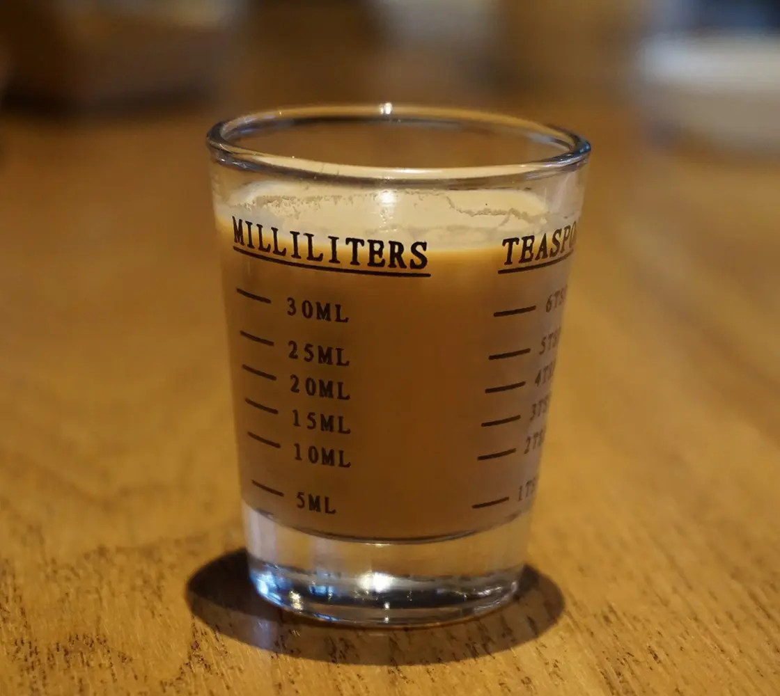 Glass measuring shot glass with milliliter markings filled with beverage